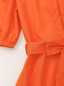 Détail d'une robe orange élégante avec manches bouffantes et ceinture en tissu nouée