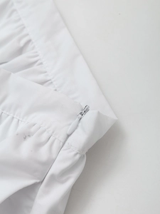 Detail of the high-waisted white skirt featuring a hidden side zipper and pleated waist