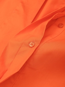 Détail du chemisier orange vif montrant les coutures soignées et le bouton en résine assorti