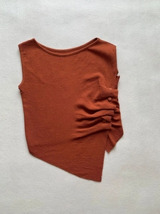 Detail view of brick red knitted top featuring side ruching and asymmetric hem design