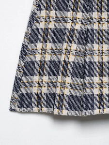 Détail du tissu en tweed sur l'ourlet de la jupe plissée avec un motif à carreaux bleu et jaune