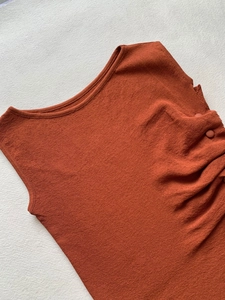 Detailed close-up of burnt orange knit top featuring side ruching and tonal buttons