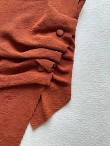 Close-up of fabric-covered buttons and fine knit texture on brick red short sleeve top
