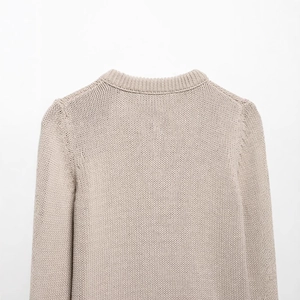 Close-up of beige chunky knit cardigan showing ribbed crew neck and textured shoulder seams