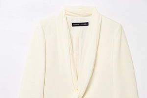 Detail view of cream shawl collar blazer showing draped neckline and interior brand label