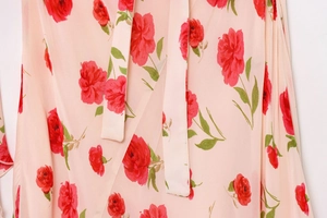 Close-up detail of pink chiffon fabric with red rose floral print and delicate neck tie