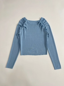 Dettaglio del top in maglia celeste con pieghe sulle spalle e bottoni decorativi
