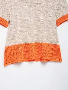 Close-up of contrast knit sweater featuring cream mesh texture and orange hem stripes
