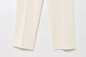 Close-up of cream straight-leg trousers showing premium fabric texture and sharp ironed crease