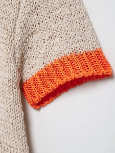 Detail view of beige chunky knit sweater with vibrant orange ribbed cuffs and texture