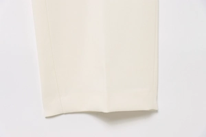 Detailed macro view of cream-colored trouser hem with clean stitching and premium fabric texture