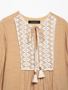 Close-up of khaki V-neck dress with white lace crochet stitching and tassel ties