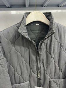 Detail of dark grey quilted jacket with wavy patterns, stand collar and metal zipper