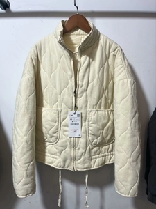 Close-up of off-white quilted jacket featuring a stand collar and metallic front zipper