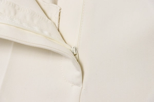 Detailed close-up of a concealed zipper and neat stitching on beige tailored trousers