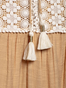 Detail of white lace crochet pattern and ginger fabric with golden tassel strings