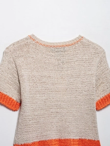 Detail of beige knit top featuring chunky texture and vibrant orange contrast edges