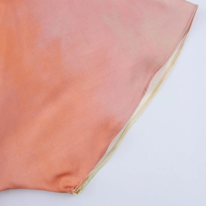 Détail du tissu satiné montrant le dégradé orange et la couture fine de l'ourlet