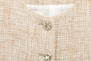 Detailed close-up of apricot tweed texture with golden twisted metal buttons on neckline