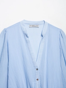 Détail d'une blouse en mousseline rayée bleu ciel avec col en V et boutons marrons