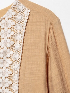 Detailed macro shot of white lace embroidery on a ginger yellow textured cotton dress