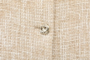 Close-up of tweed fabric texture with gold metallic button and shimmering gold threads