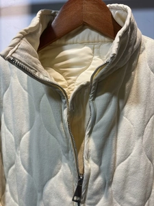 Detail of onion quilted vest featuring metal zipper and high stand collar in ivory