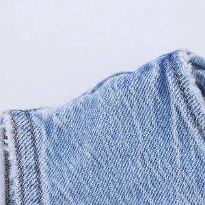 Détail du tissu denim bleu avec coutures orange et bordure à franges effilochées