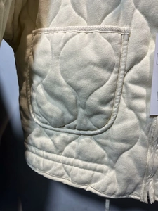 Detail of cream quilted jacket featuring curved stitching patterns and large patch pockets