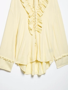 Detail of light yellow chiffon shirt featuring ruffled V-neckline and elegant tie closure