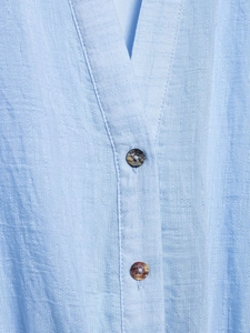 Détail du chemisier texturé bleu clair à col en V avec boutons à effet marbre foncé