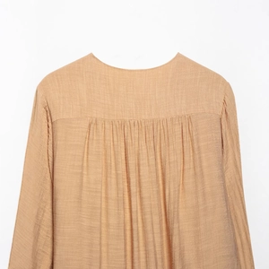 Back view of a loose khaki long-sleeve blouse featuring pleated yoke and textured fabric