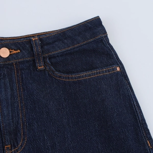 Détail d'un jean bleu foncé à taille haute avec des coutures contrastées orange