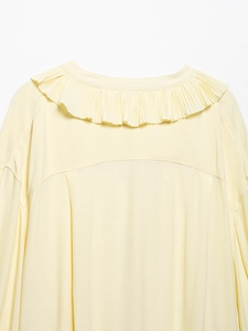 Detail view of the elegant pleated V-neckline and textured yellow fabric of the blouse