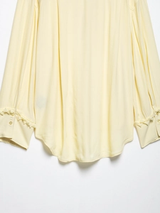 Detail showing ruffled cuffs and rounded hemline of the cream-colored V-neck blouse