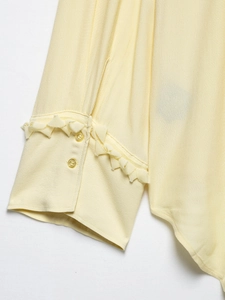 Close-up of ruffled cuff detail and fabric texture on a cream-colored V-neck blouse