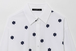 Detail of white cotton poplin shirt with blue floral embroidery and classic collar