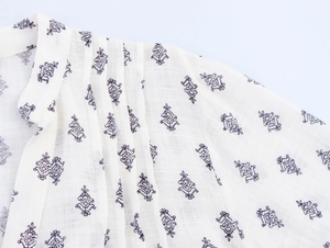 Close-up of pleated shoulder details and floral print on a white cotton blouse