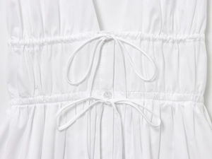 Macro shot of white summer dress featuring elastic waist with drawstring bows and buttons