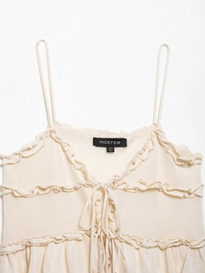 Détail d'un caraco en maille beige avec volants superposés et nœud décoratif devant