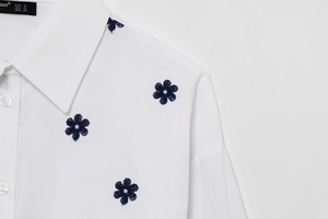 Detailed close-up of floral embroidery on a white poplin cotton shirt with brand label