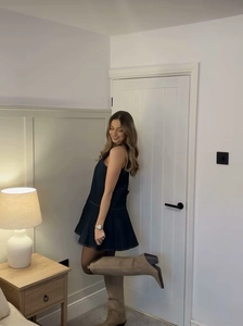 Détail d'une robe en denim sans manches bleu foncé avec ourlet plissé et bottes montantes