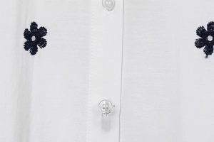 Detail of floral embroidery and resin buttons on white poplin cotton shirt