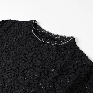 Close-up detail of black floral lace fabric with mock neck and ruffled edge on top
