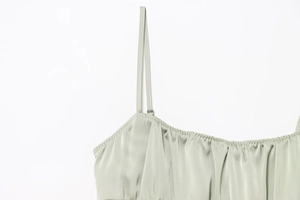 Macro detail of sage green satin fabric with delicate pleats and thin spaghetti straps