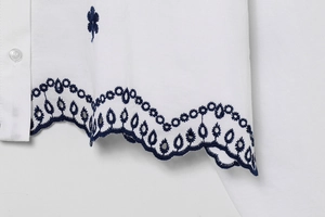 Detailed close-up of blue floral embroidery and scalloped hem on white cotton shirt
