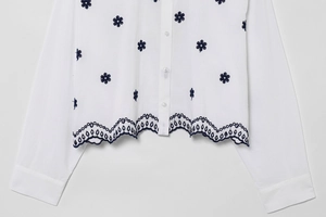 Detailed view of floral embroidery and navy scalloped lace hem on white poplin shirt