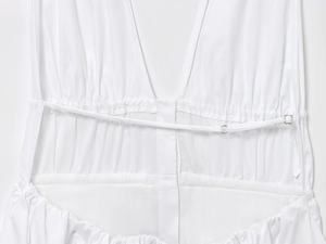 Detail view of white backless dress featuring thin adjustable straps and waist smocking