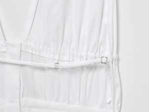 Detail of white dress with drawstring ties, silver metal ring, and pleated fabric texture