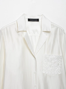 Close-up of white satin shirt with delicate vine embroidery on the front pocket